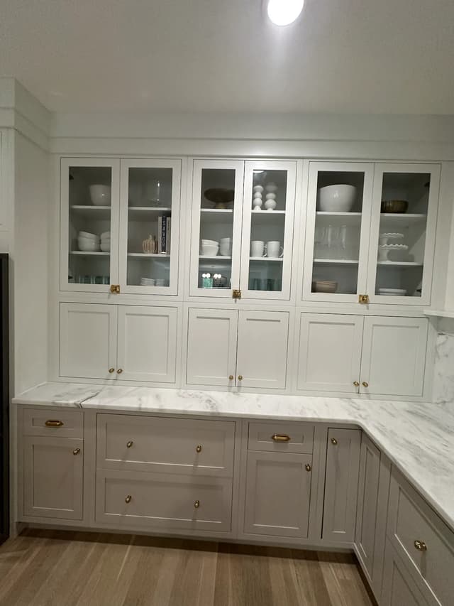 Glass-front white cabinetry above layered greige storage
