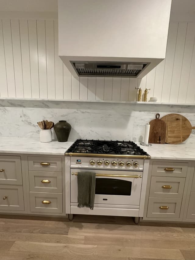 Soft greige range cabinetry with marble backsplash and brass details