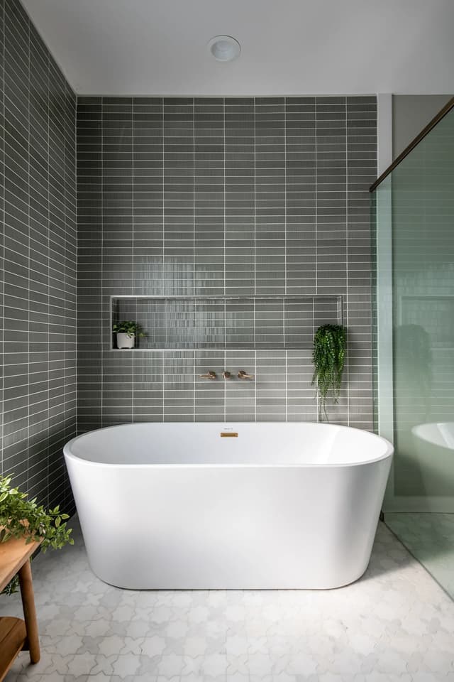 Freestanding soaking tub framed by sage tile and a recessed shelf