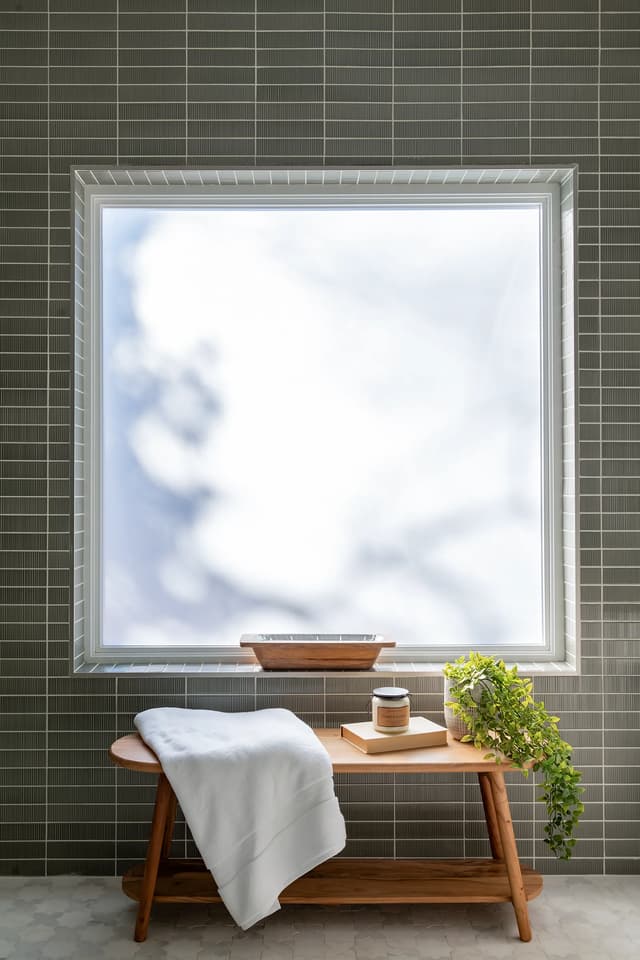 Spa bench beneath a bright window surrounded by sage tile